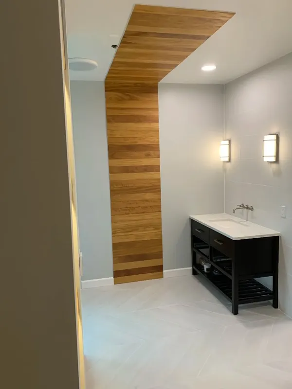 Modern Bathroom Feature Wall — Herringbone stone floor with wood-look planks wrapping from wall to ceiling for a seamless architectural detail.
