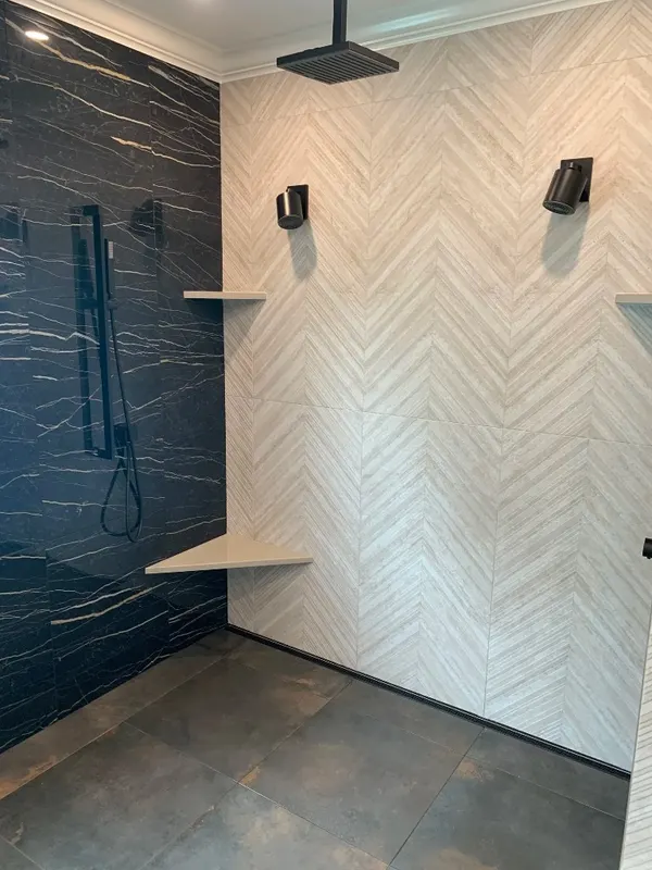 Spa-Inspired Bathroom — Chevron stone walls, black marble feature wall, freestanding tub, and etched tropical window detail.