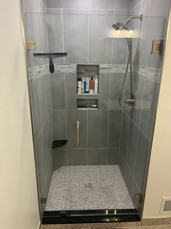 Modern Grey Shower with Terrazzo Floor — Large-format grey wall tile with a glass mosaic accent band, double niche, and speckled terrazzo shower floor.