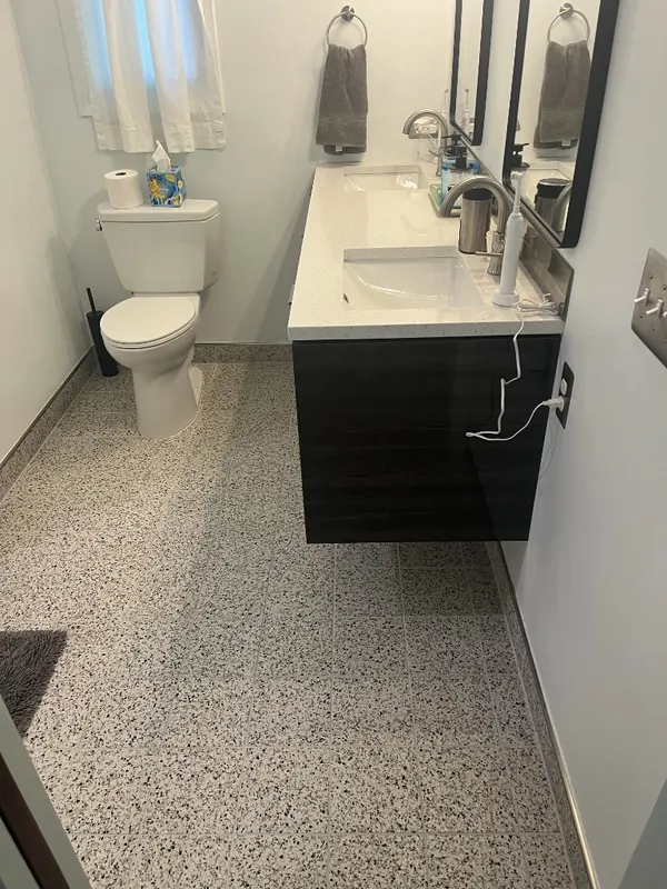 Terrazzo Bath with Floating Vanity — Speckled terrazzo flooring carried wall to wall beneath a floating vanity, with a tiled baseboard detail.