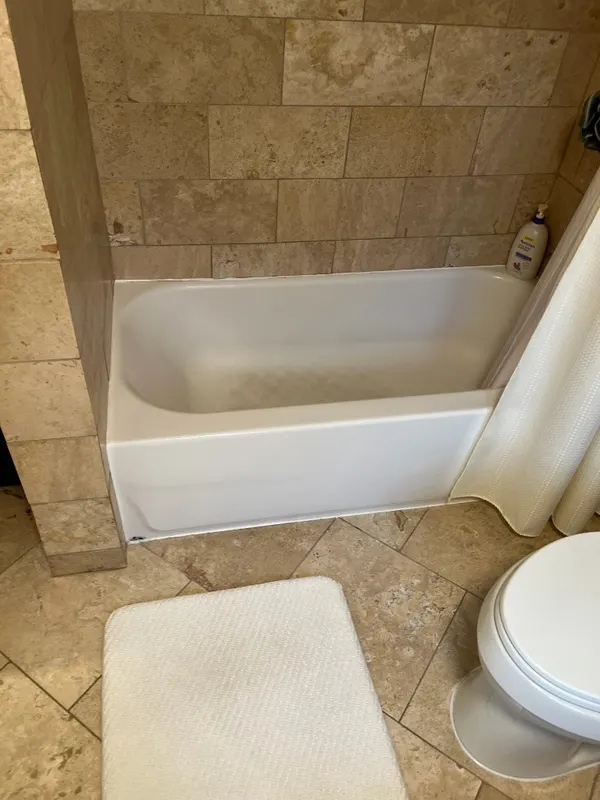 Travertine Tub Surround — Natural travertine tub surround in a running-bond layout, tightly fitted to the tub deck and floor tile.
