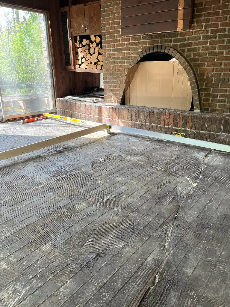 Prepared concrete slab with levels and a long straightedge checking flatness across the room