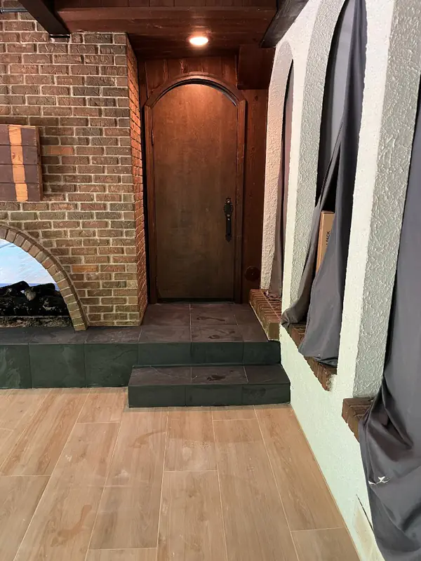Finished entry with slate steps and wood-look plank flooring leading to an arched wood door