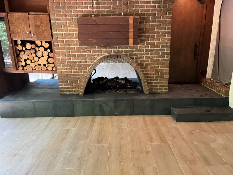 Finished wood-look plank floor meeting a dark slate hearth at the brick fireplace